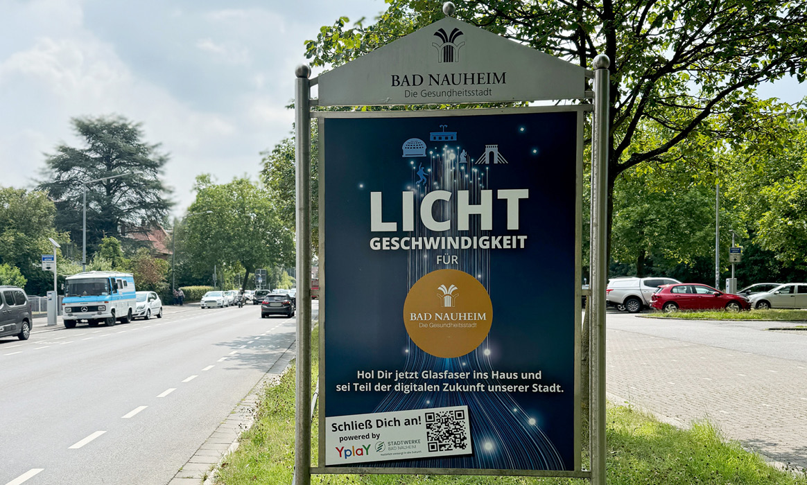Ortseingangstafel der Glasfaserkampagne der Stadt Bad Nauheim an einer Bushaltestelle mit der Überschrift „LICHT GESCHWINDIGKEIT“, dem Hinweis „BAD NAUHEIM geht online“, einem QR-Code sowie Informationen zum Glasfaserausbau.