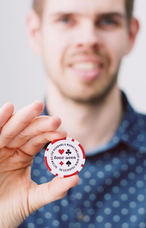 Benjamin Holzhausen in der Unschärfe hält Pokerchip in die Kamera