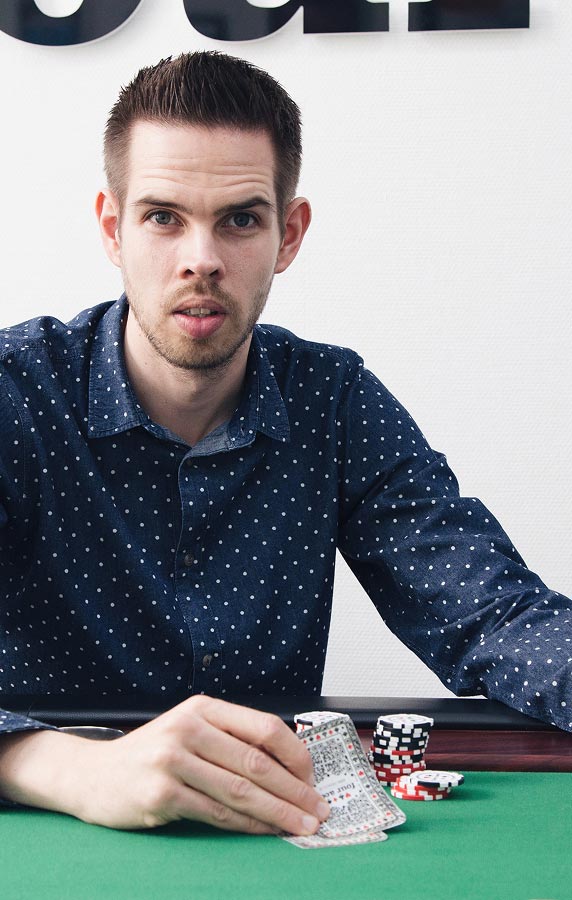 Benjamin Holzhausen schaut in die Kamera und deckt Pokerkarten auf dem Tisch auf