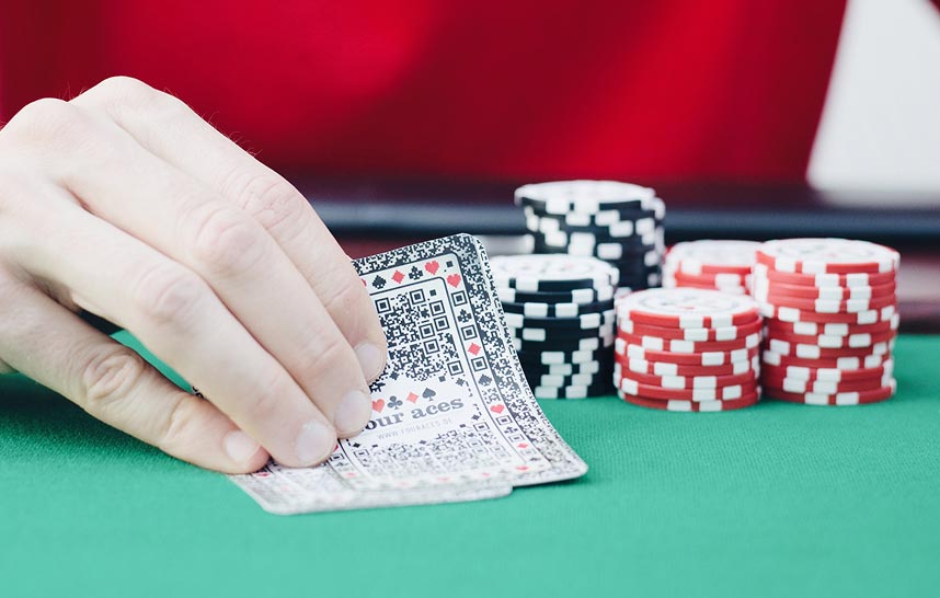Hand deckt Pokerkarten auf Pokertisch auf, im Hintergrund stapeln sich Pokerchips