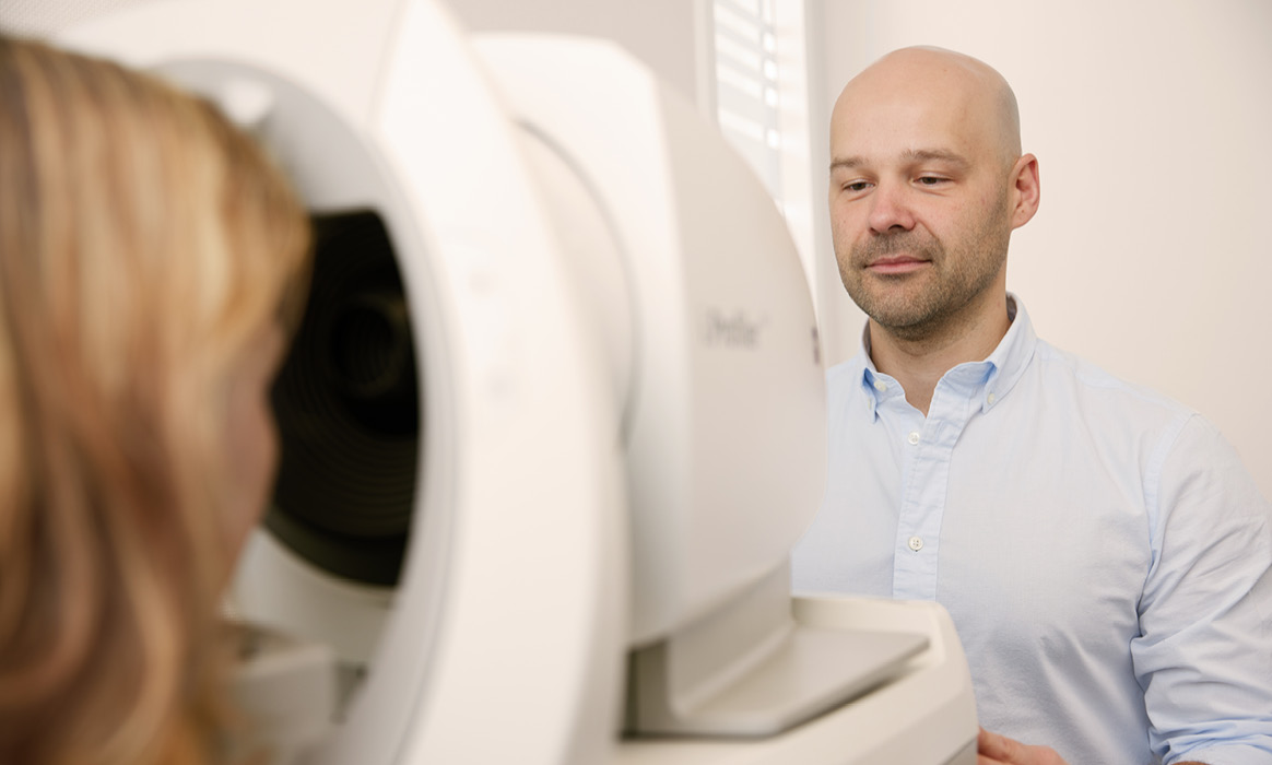 Augenmessung in einem Optikgeschäft mit einer Kundin an einem Messgerät, während ein Optiker den Sehtest begleitet.