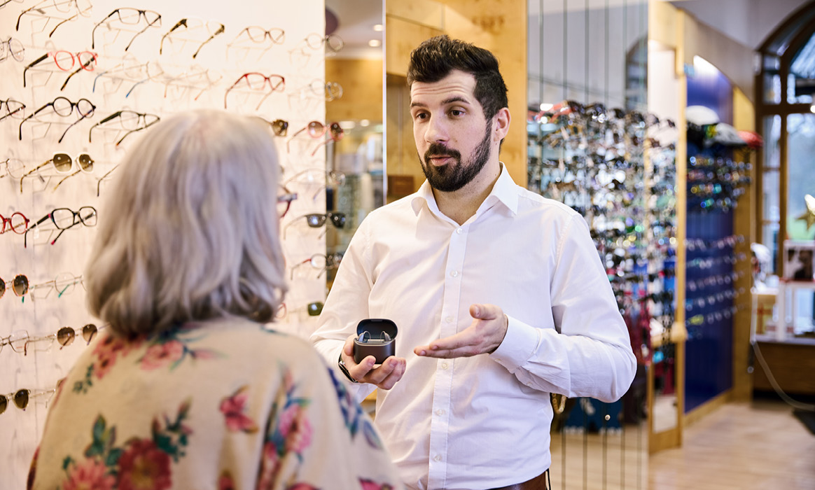 Beratungsgespräch bei Optik Boelke mit einem Optiker, der einer Kundin eine Brillenfassung präsentiert. Im Hintergrund sind ausgestellte Brillenfassungen zu sehen.