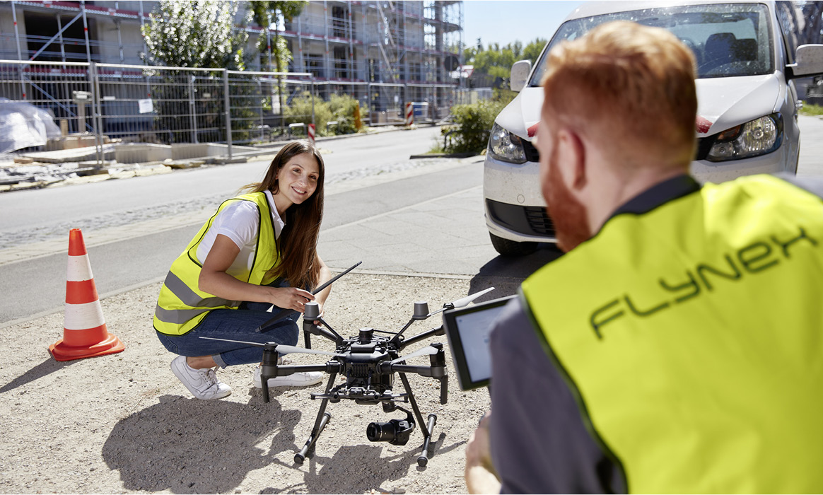 Zwei Mitarbeitende von FlyNex bereiten eine Drohne auf einer Baustelle für den Einsatz vor.