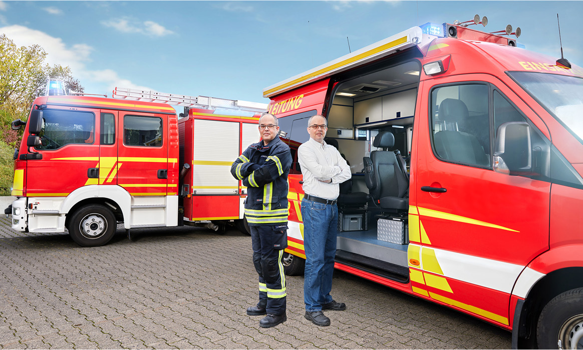 Businessfotografie der Geschäftsführung von IDH vor zwei Einsatzfahrzeugen der Feuerwehr auf einem Betriebshof.