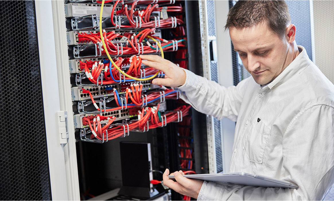 Mitarbeiter von IDH bei der Wartung eines Serverschranks mit Netzwerktechnik und Verkabelung.